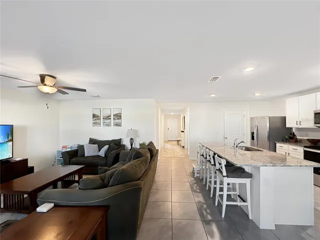 a living room with stainless steel appliances furniture a rug and a kitchen view