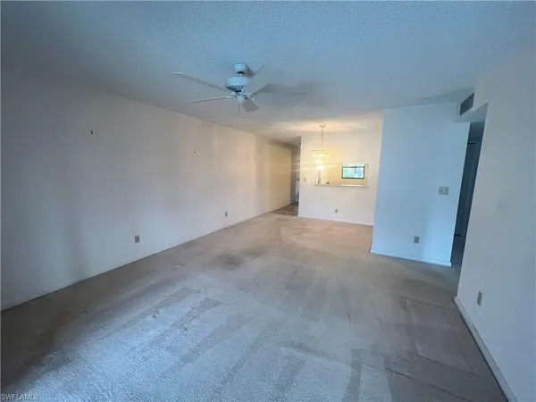 an empty room with chandelier fan and windows