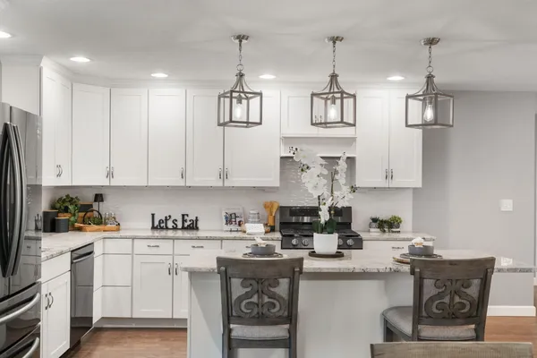 a kitchen with stainless steel appliances granite countertop a refrigerator a sink dishwasher a stove and white cabinets with wooden floor