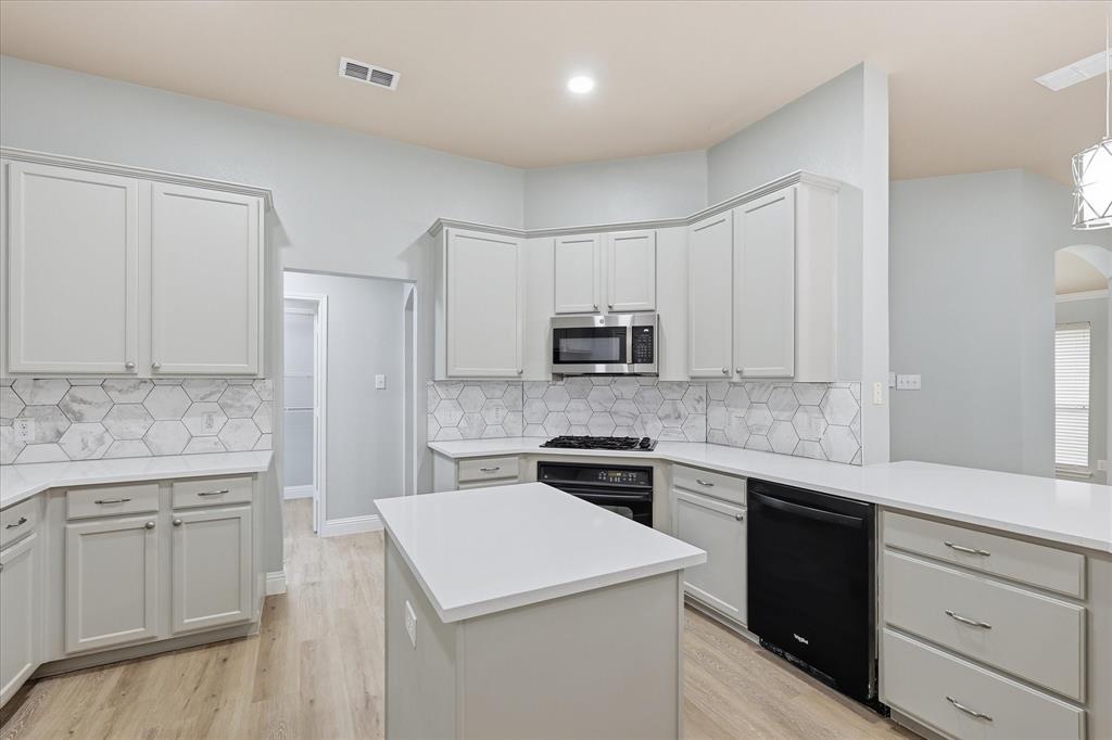 2616 Hollow Ridge Drive Denton, TX 76210 - Photo 12 of 31 Modern kitchen featuring a central island, light-toned cabinetry, light wood-finish flooring, white countertops, and a white hexagonal tile backsplash