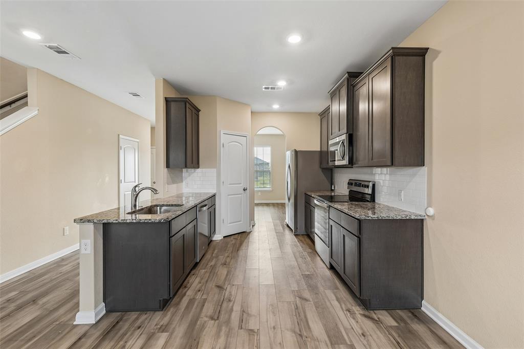 230 Enchanted Way Princeton, TX 75407 - Photo 4 of 31 a kitchen with stainless steel appliances granite countertop a stove top oven a sink dishwasher a refrigerator and cabinets with wooden floor