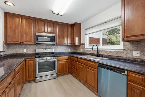 a kitchen with stainless steel appliances granite countertop wooden cabinets a stove top oven a sink and dishwasher