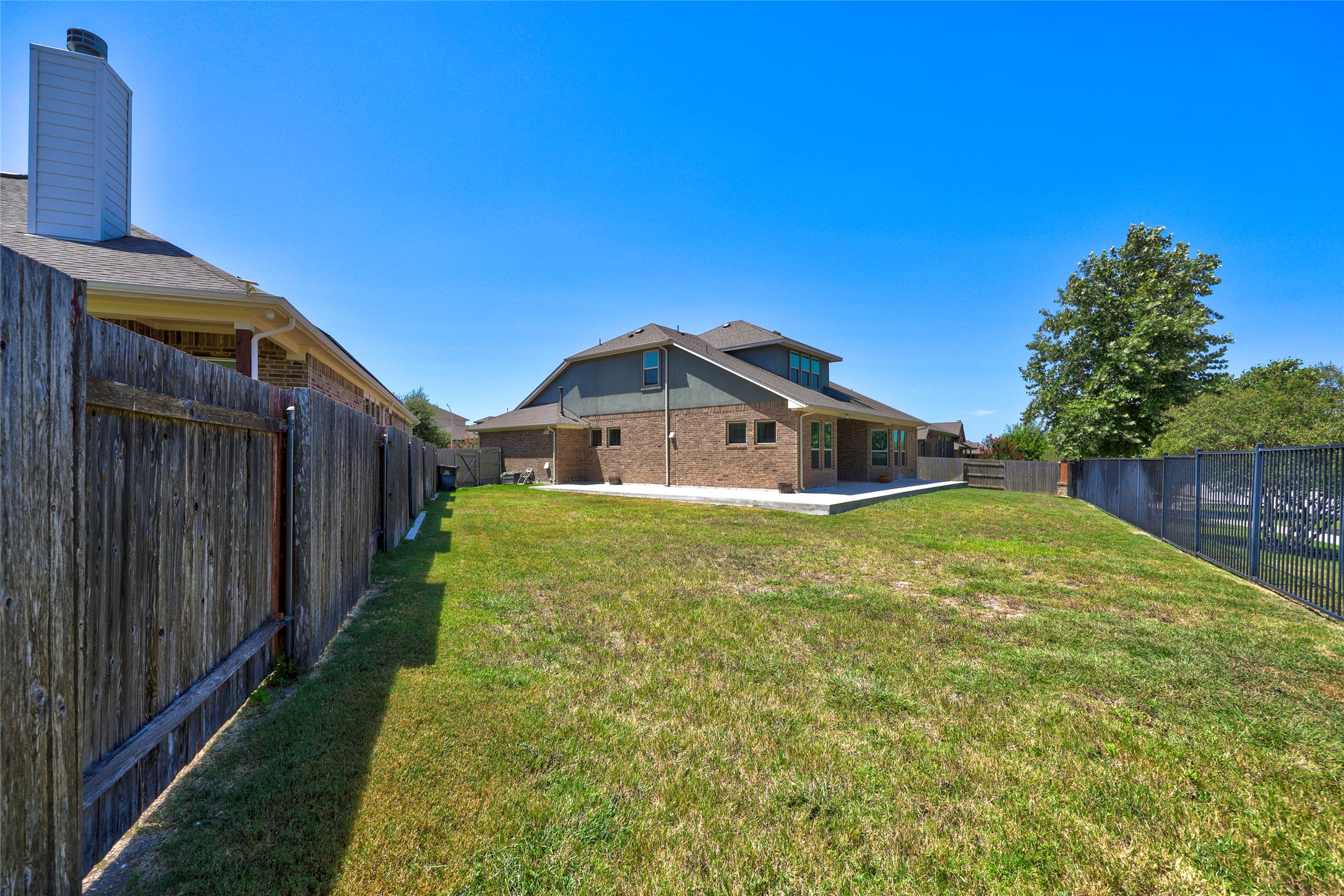 409 Betony Loop Buda, TX 78610 - Photo 30 of 38 A spacious backyard with mature trees and a brick-and-siding home, perfect for outdoor living.