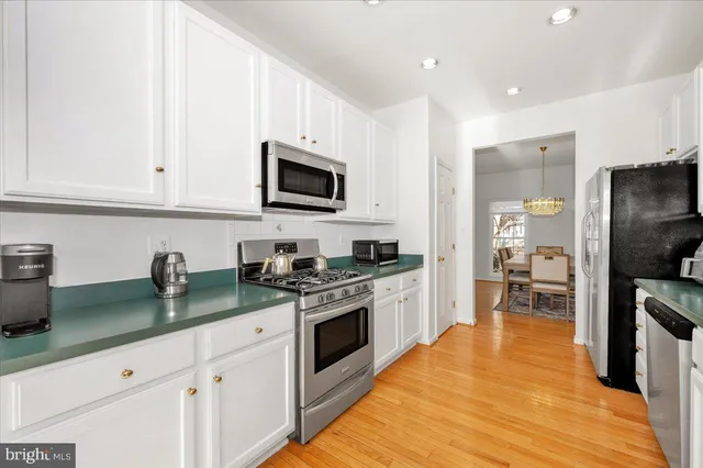 a kitchen with stainless steel appliances granite countertop a stove top oven a sink a refrigerator white cabinets and wooden floor