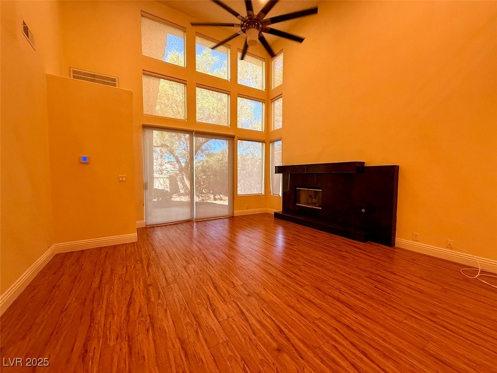 4969 Jeremy Drive Las Vegas, NV 89113 - Photo 12 of 73 Unfurnished living room featuring a tiled fireplace, light wood-type flooring, a ceiling fan, and a towering ceiling