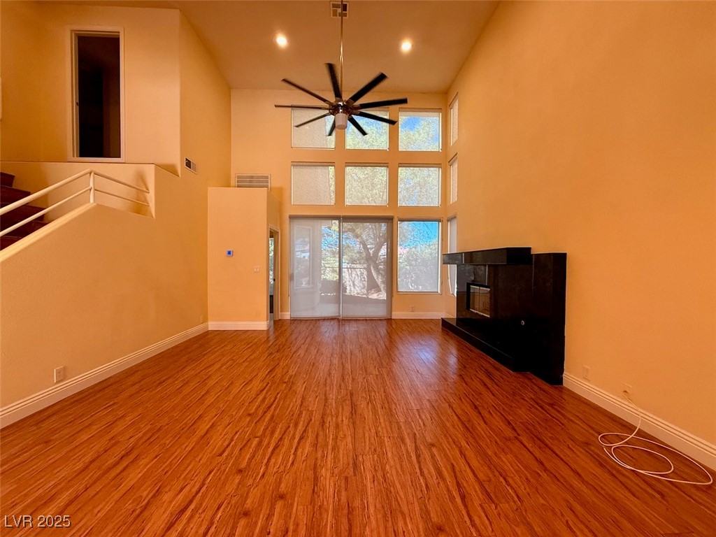 4969 Jeremy Drive Las Vegas, NV 89113 - Photo 10 of 73 Unfurnished living room featuring wood finished floors, ceiling fan, a fireplace, a towering ceiling, and recessed lighting