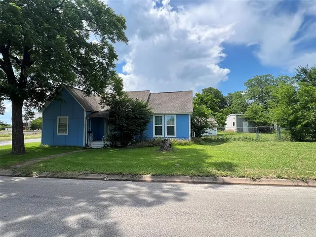 a tall tree in middle of green field in front of house