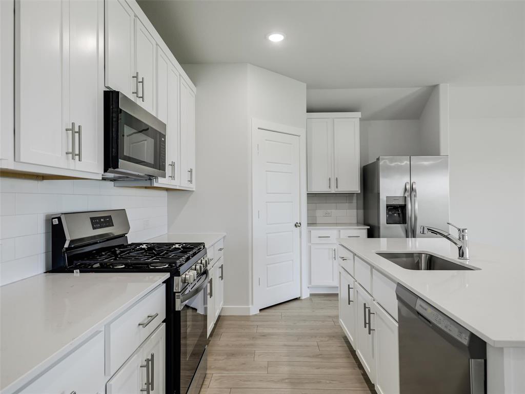 1136 Del Rio Drive Lavon, TX 75166 - Photo 5 of 30 Modern kitchen featuring white cabinetry, light countertops, stainless steel appliances, a subway tile backsplash, and wood-finish flooring