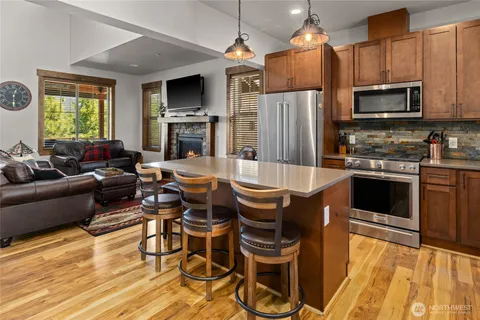 a kitchen with stainless steel appliances granite countertop a stove top oven a sink dishwasher a dining table and chairs with wooden floor