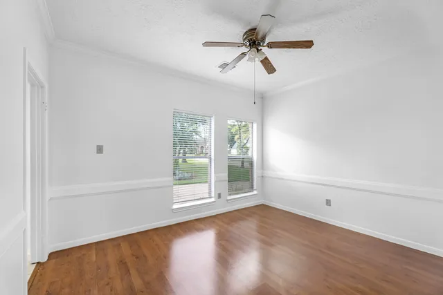 a view of an empty room with wooden floor and a ceiling fan