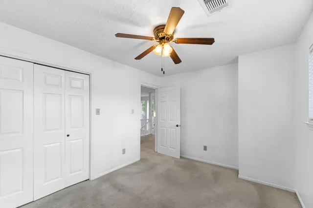 an empty room with chandelier fan and windows