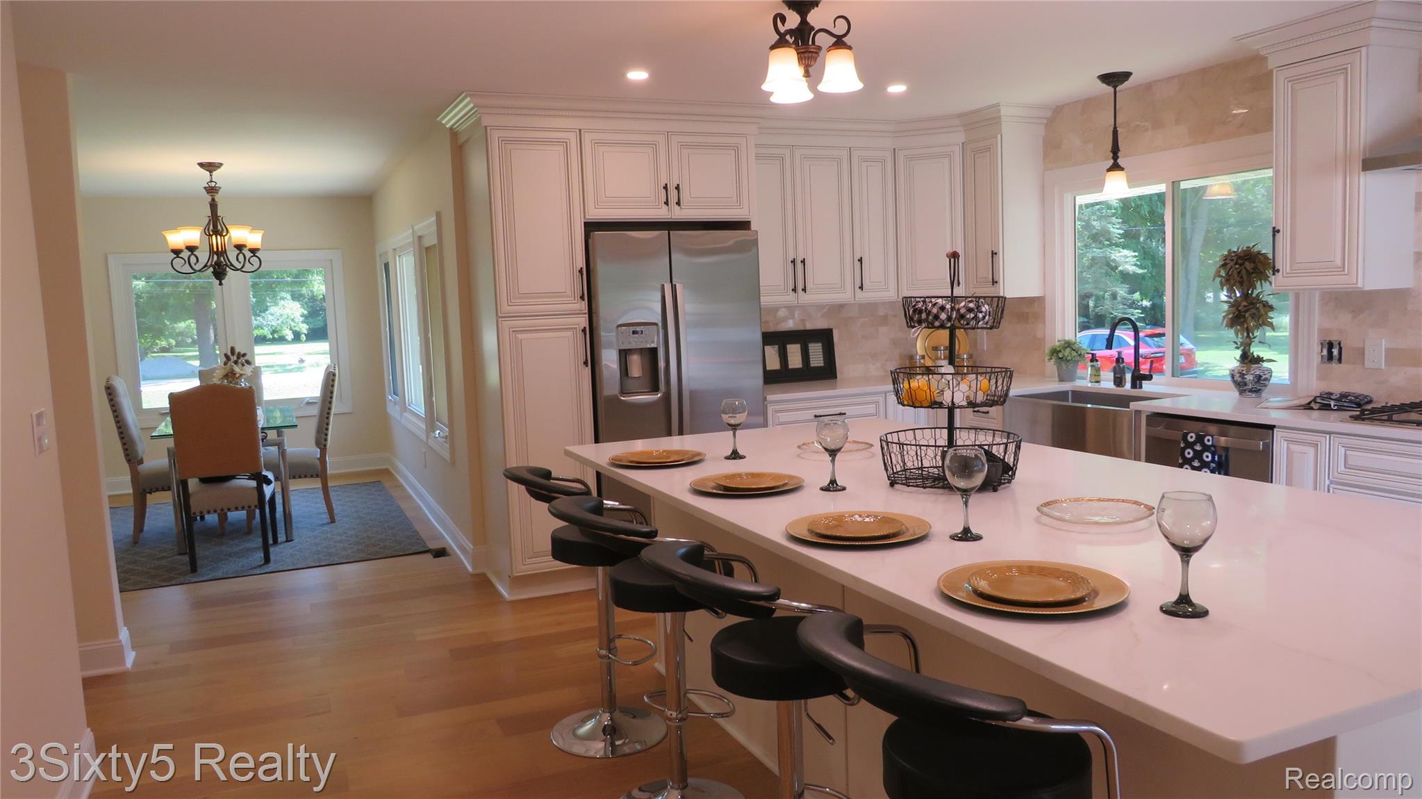 16558 Haggerty Road Belleville, MI 48111 - Photo 15 of 40 Kitchen featuring white cabinetry, stainless steel appliances, a large center island with seating, a stainless steel farmhouse sink, and a tiled backsplash
