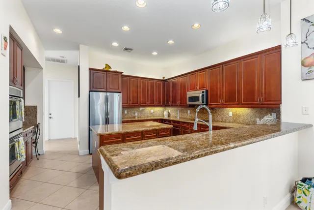 a kitchen with stainless steel appliances granite countertop a refrigerator a stove and a sink with wooden cabinets
