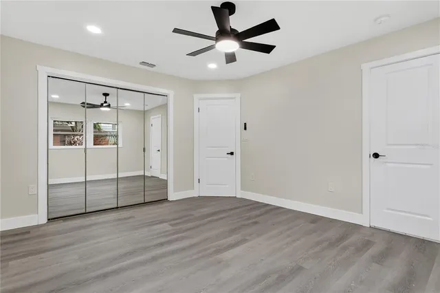a view of an empty room with wooden floor and a ceiling fan