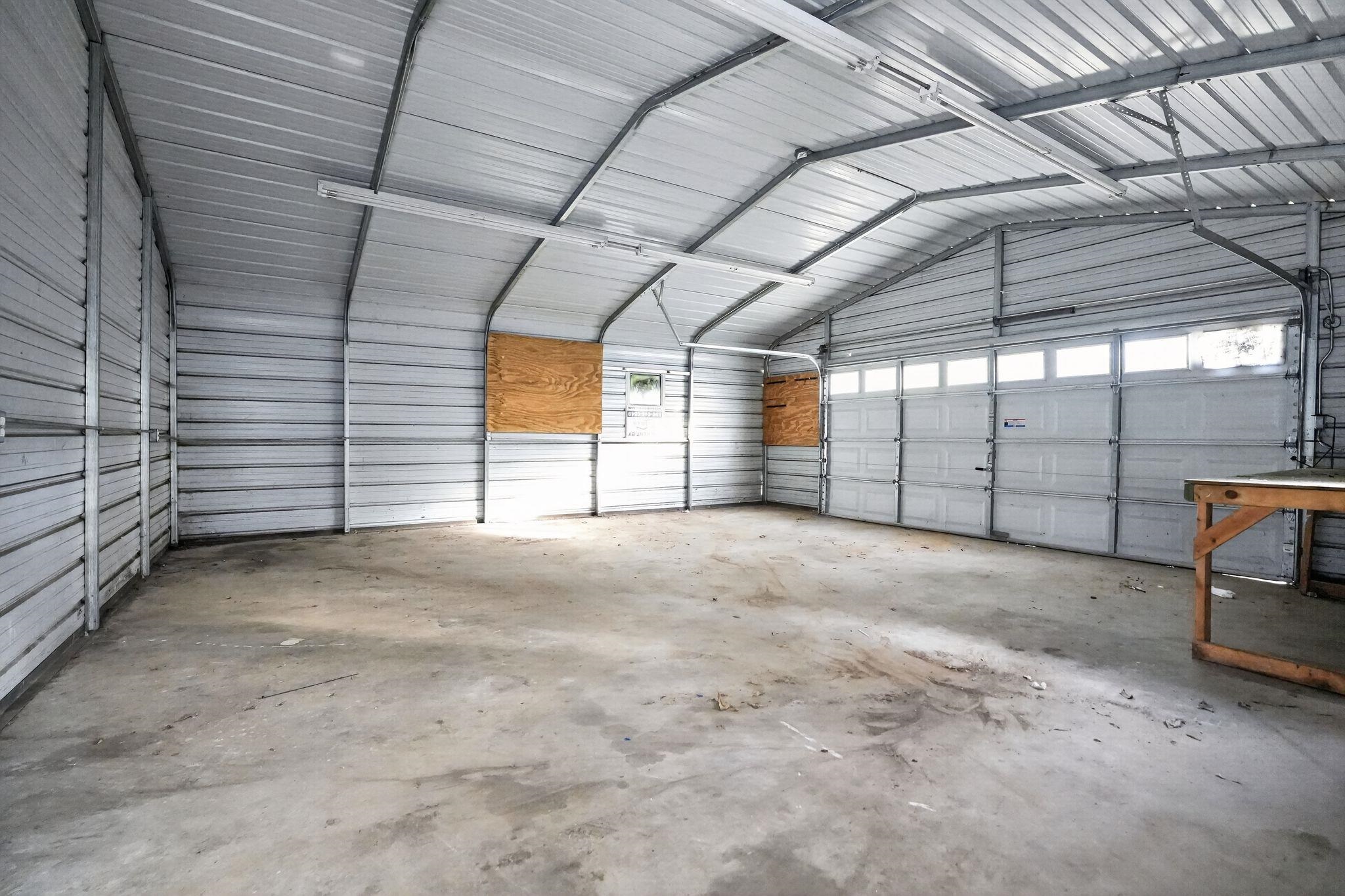 4199 Auburn Road Memphis, TN 38116 - Photo 6 of 32 Spacious corrugated metal structure featuring a concrete floor, multiple fluorescent light fixtures, and a large garage door with transom windows