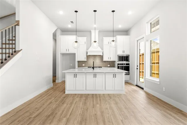 a large kitchen with stainless steel appliances kitchen island granite countertop a stove a sink a refrigerator white cabinets and wooden floor