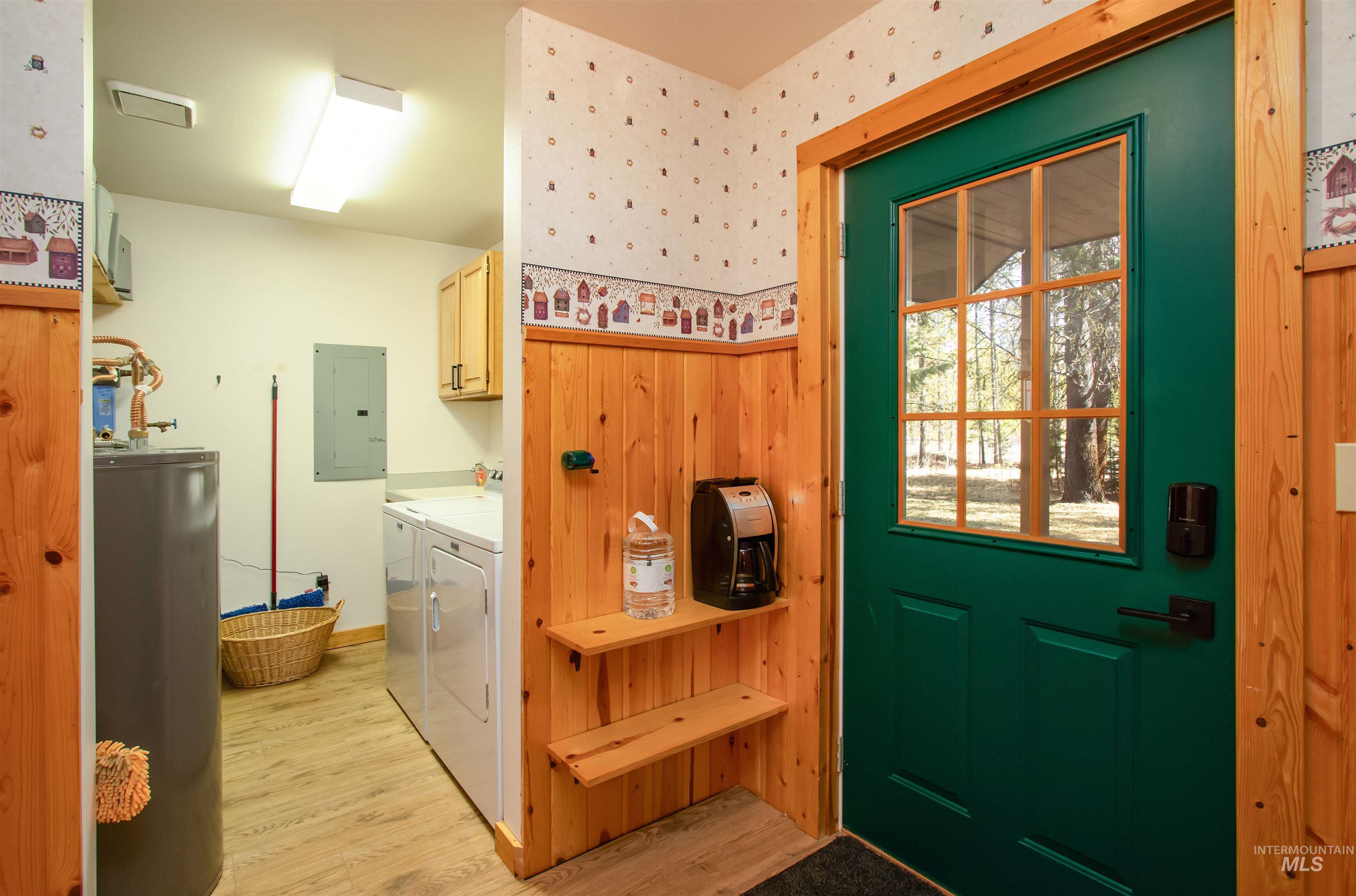 12712 Hereford Road Donnelly, ID 83615 - Photo 20 of 50 Doorway to outside featuring water heater, wood finished floors, separate washer and dryer, electric panel, and wallpapered walls