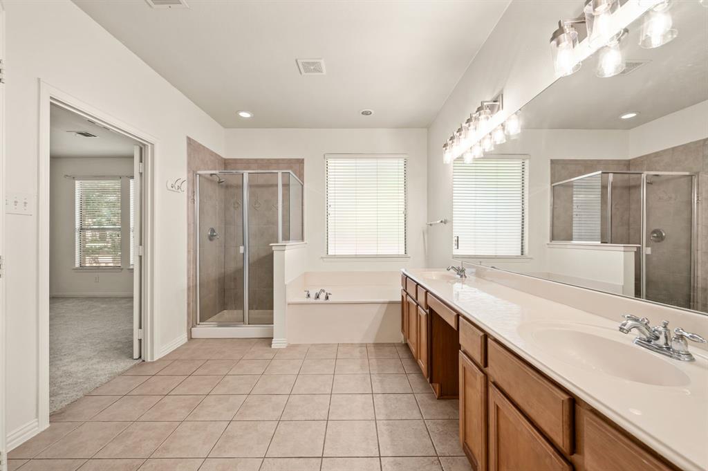808 Briar Ridge Drive Keller, TX 76248 - Photo 19 of 40 Spacious bathroom featuring dual vanities with integrated sinks, a wide mirror with overhead lighting, a glass-enclosed shower, a built-in bathtub, and tile flooring