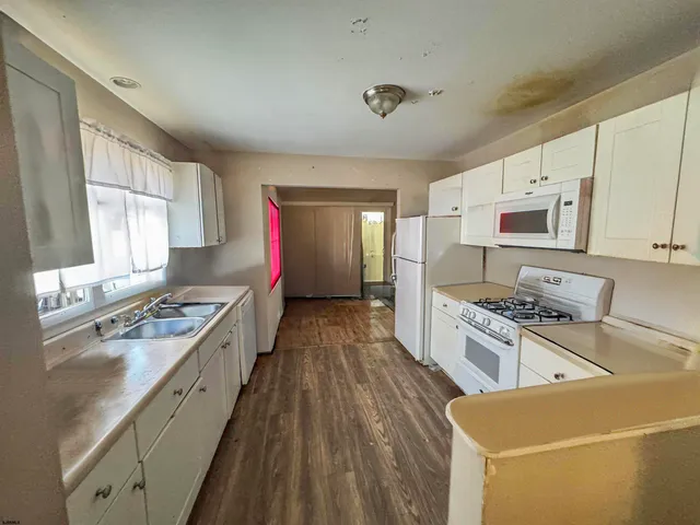 a kitchen with stainless steel appliances a stove top oven a sink a refrigerator white cabinets and wooden floor