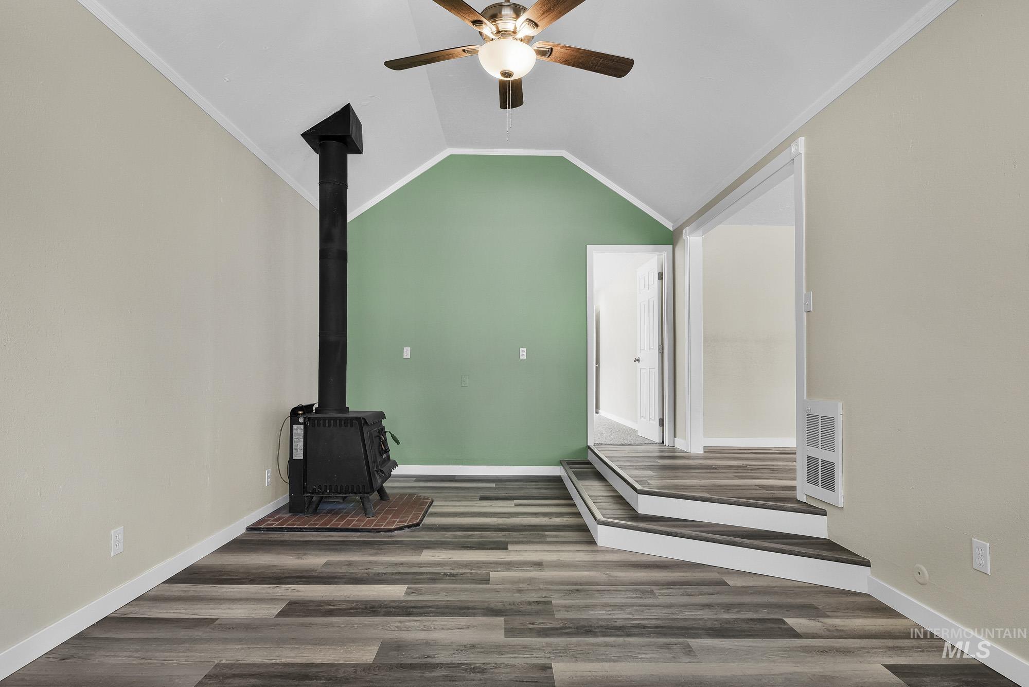 5755 Chuckwagon Road Nampa, ID 83686 - Photo 5 of 50 Wood-finish flooring, accent wall, vaulted ceiling, wood-burning stove with brick hearth, and ceiling fan with integrated lighting