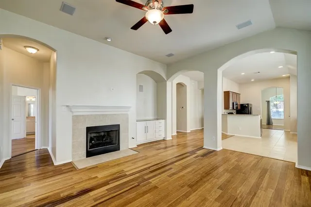 a view of a livingroom with a fireplace a ceiling fan and wooden floor