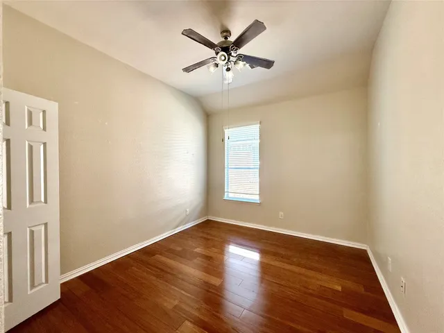 an empty room with wooden floor fan and windows