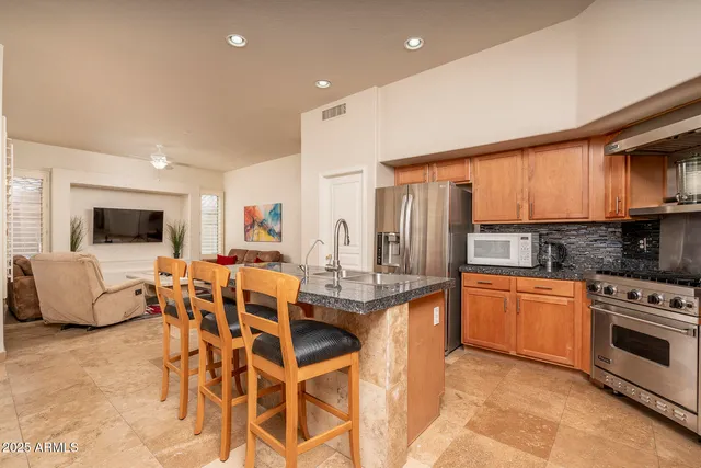 a view of kitchen with stainless steel appliances granite countertop dining table chairs sink and cabinets