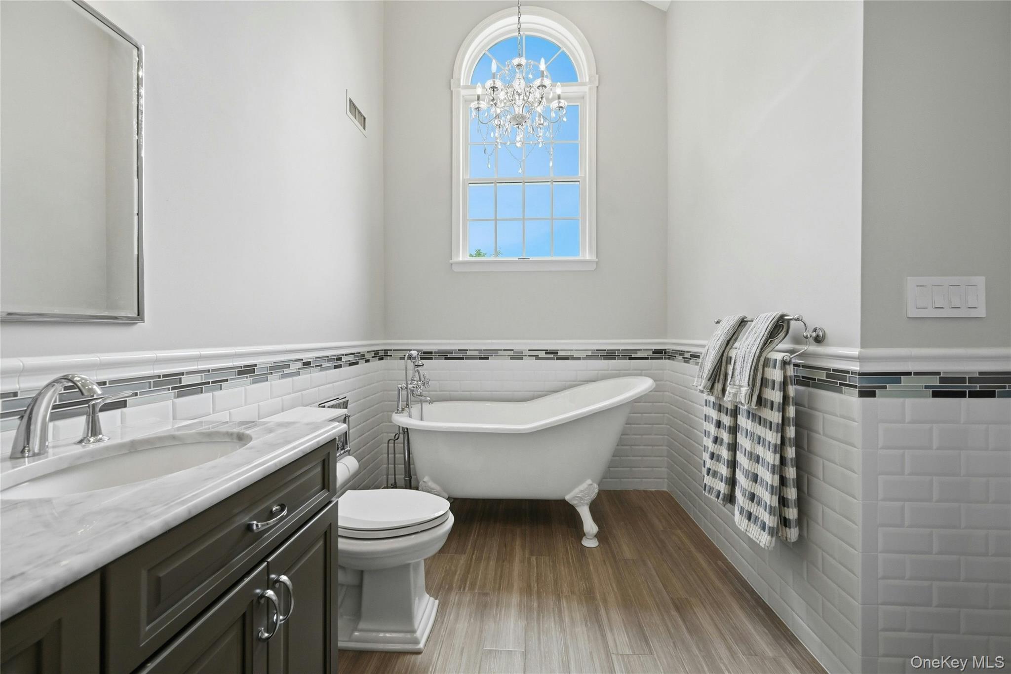 6 Thunder Road Miller Place, NY 11764 - Photo 26 of 50 The Primary Bathroom Is A Page Out Of Architectural Digest Magazine - A Stunning Free Standing Antique Style Tub With High End Fixtures, Soaring Ceilings With An Accent Circle Topped Window & Chandelier, Oversized Custom Shower With Classic Subway Tiled Walls & Wraparound Frameless Glass Doors (Original Walls Removed When The Bathroom Was Redesigned), All Subway Tiled Walls With Decorative Borders, Custom Dual Sink Marble Topped Vanity, Porcelain Plank Tiled Floors & All Upgraded Fixtures...A True Showplace.
