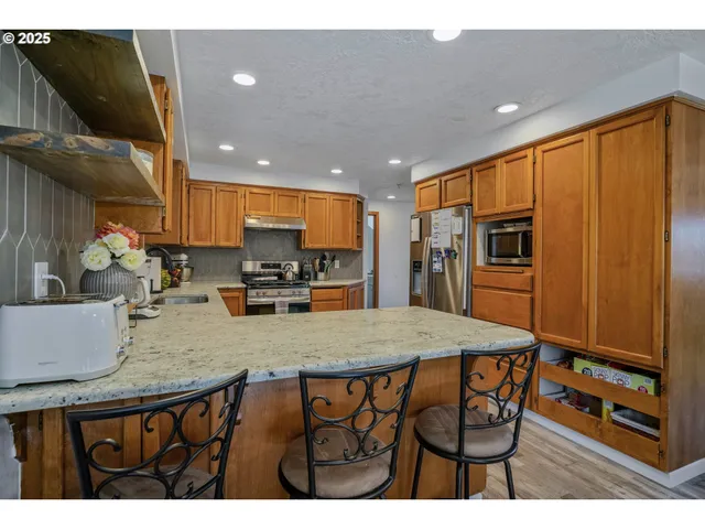 a kitchen with stainless steel appliances granite countertop a refrigerator a sink a stove a dining table and chairs