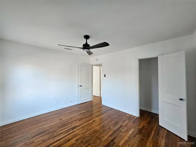 a view of a big room with wooden floor ceiling fan and windows