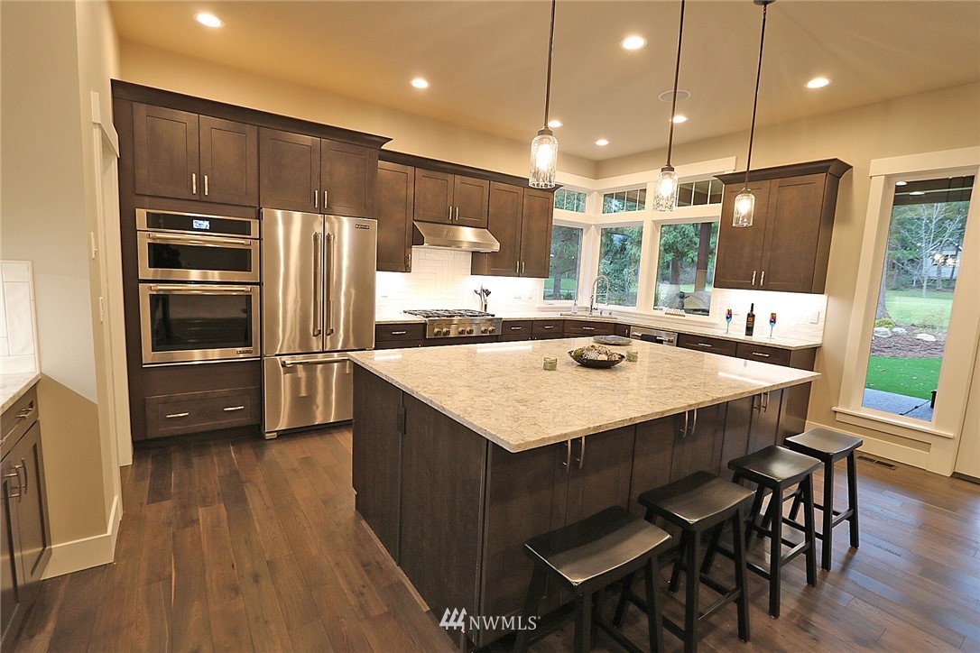 8826 Goshawk Road Blaine, WA 98230 - Photo 4 of 24 a kitchen with kitchen island a refrigerator a stove a sink and a dining table with wooden floor