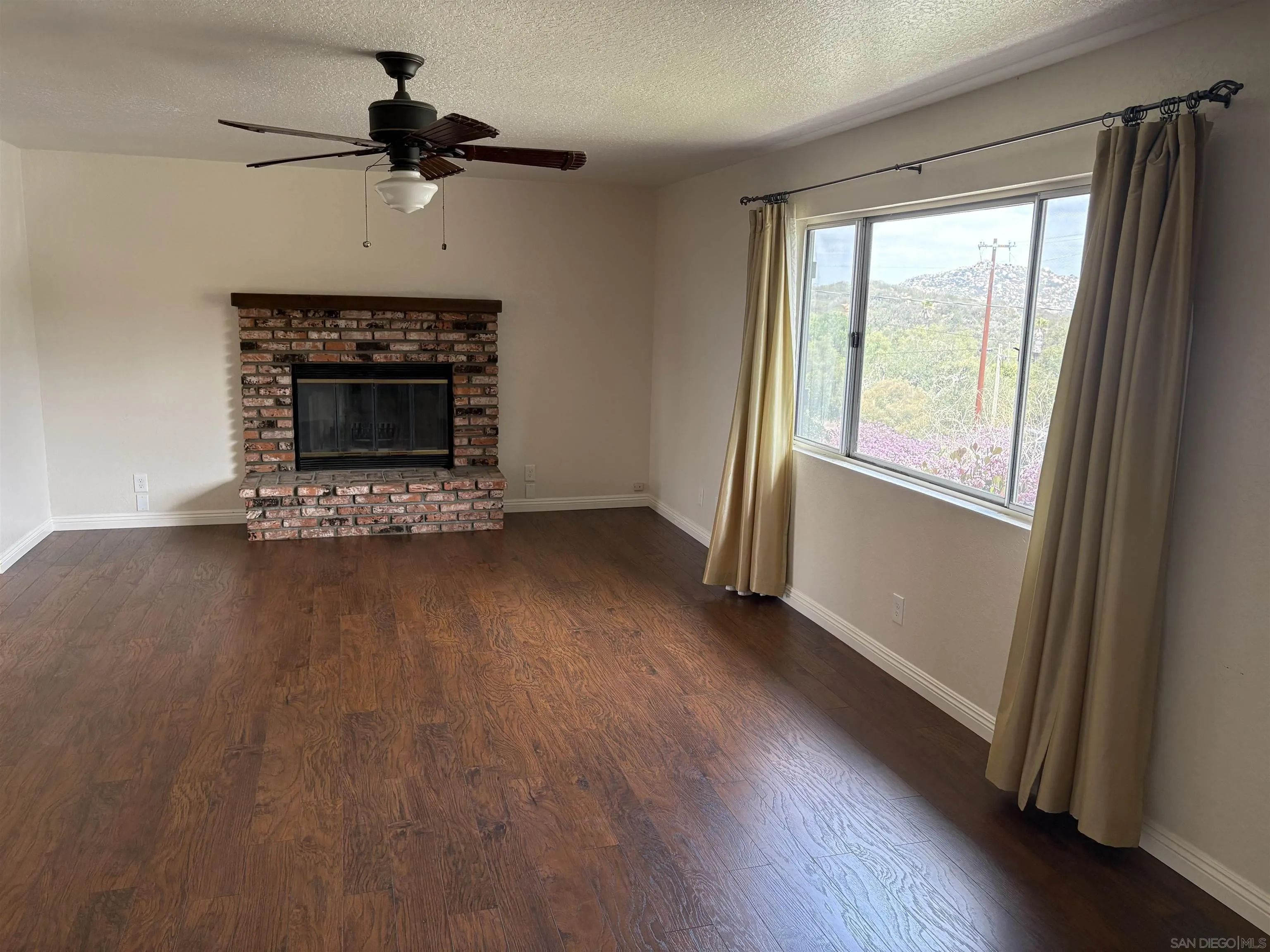 6702 Rainbow Heights Road Rainbow, CA 92028 - Photo 20 of 37 an empty room with wooden floor a fireplace and windows