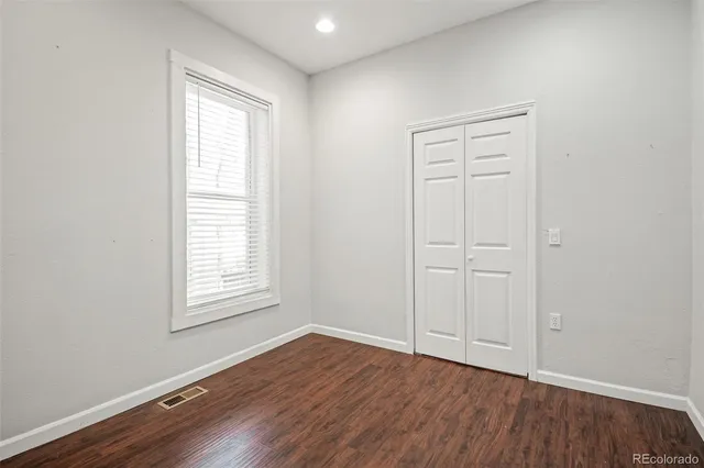 an empty room with wooden floor closet and windows
