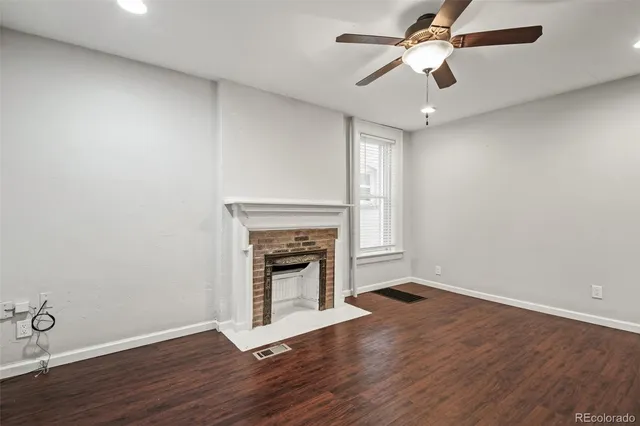 an empty room with wooden floor a ceiling fan and fireplace