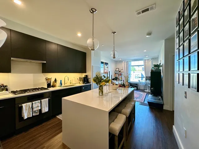 a view of a kitchen with kitchen island a stove a sink a center island wooden floor and living room view