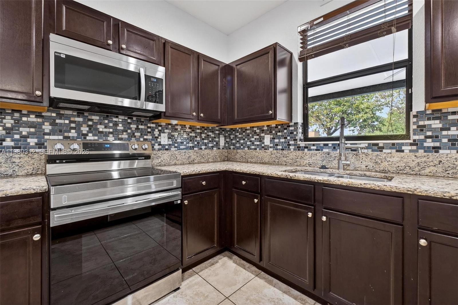 11561 Southwest 232nd Lane, Unit 11561 Homestead, FL 33032 - Photo 14 of 61 a kitchen with granite countertop wooden cabinets stainless steel appliances and a window