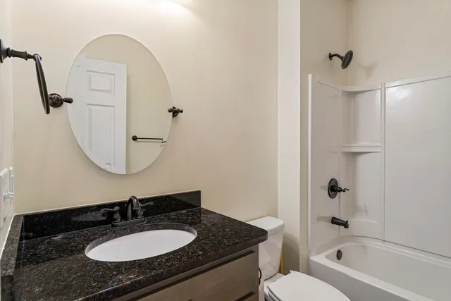 a bathroom with a granite countertop sink a toilet a mirror and shower