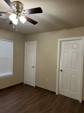 an empty room with wooden floor chandelier fan and windows