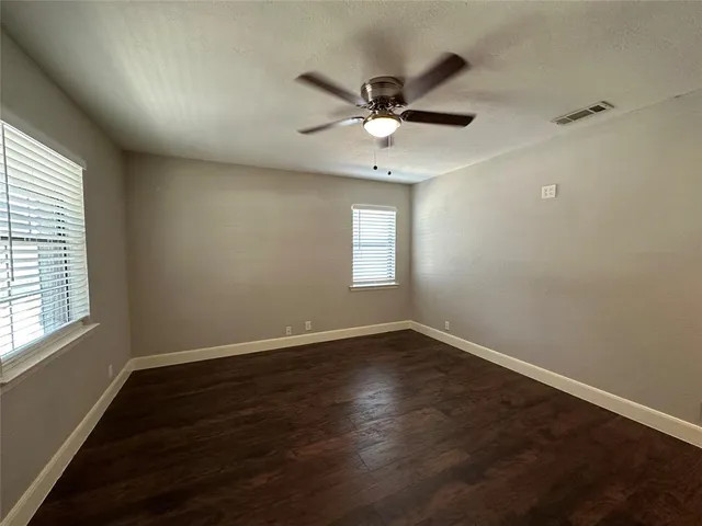 an empty room with wooden floor fan and windows