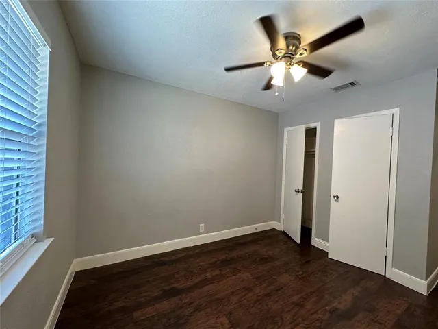 an empty room with wooden floor fan and windows
