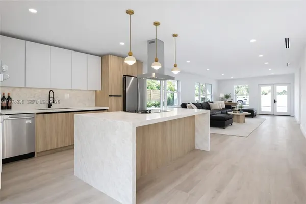 a kitchen with stainless steel appliances granite countertop a refrigerator a sink dishwasher a oven and a dining table with wooden floor