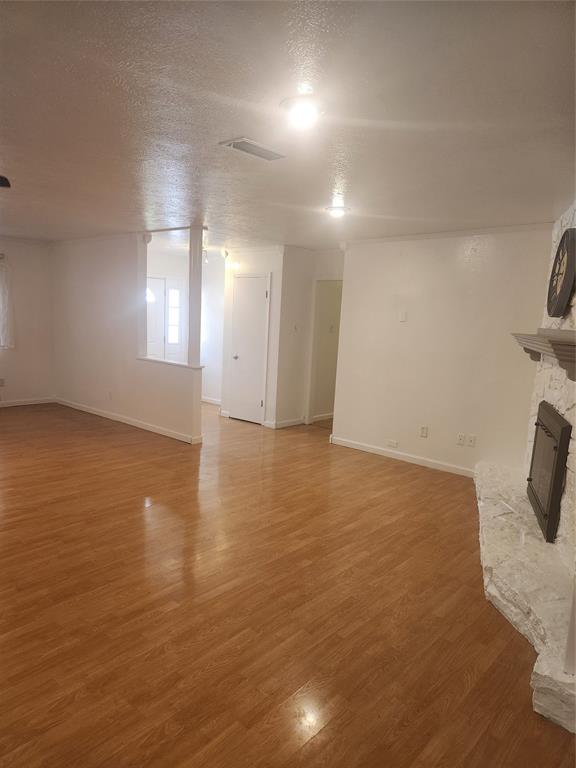12911 Mitchwin Road Farmers Branch, TX 75234 - Photo 15 of 38 Unfurnished living room with baseboards, a textured ceiling, a stone fireplace, and light wood finished floors