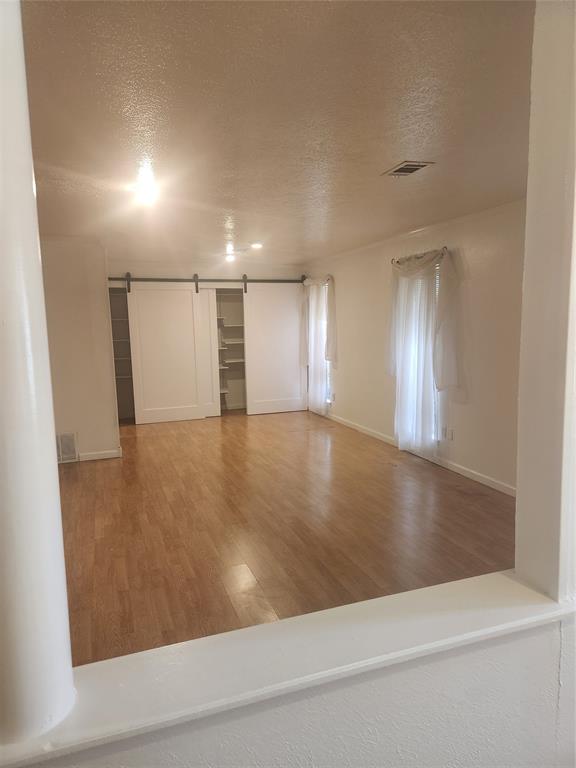 12911 Mitchwin Road Farmers Branch, TX 75234 - Photo 6 of 38 Empty room featuring a barn door, wood finished floors, visible vents, and a textured ceiling