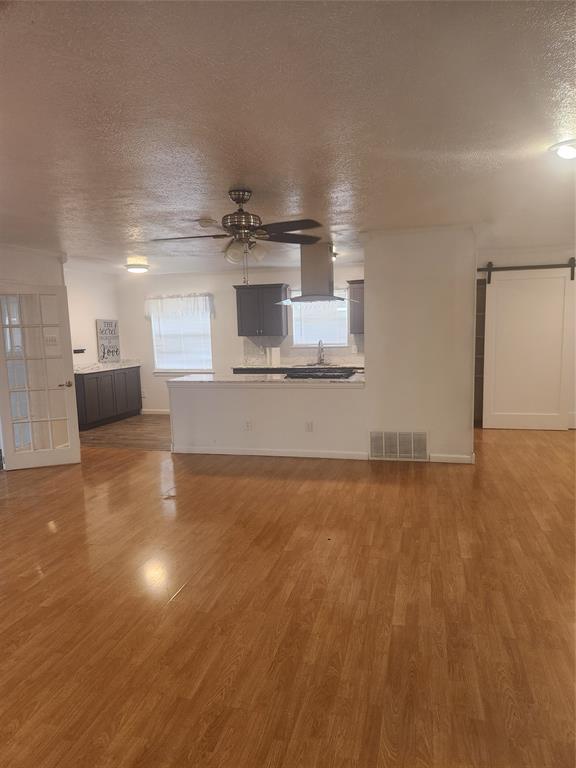 12911 Mitchwin Road Farmers Branch, TX 75234 - Photo 7 of 38 Unfurnished living room featuring visible vents, ceiling fan, a barn door, wood finished floors, and a textured ceiling