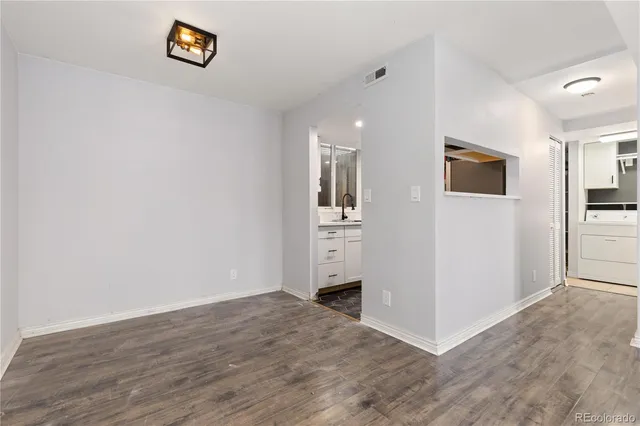an empty room with wooden floor and kitchen view