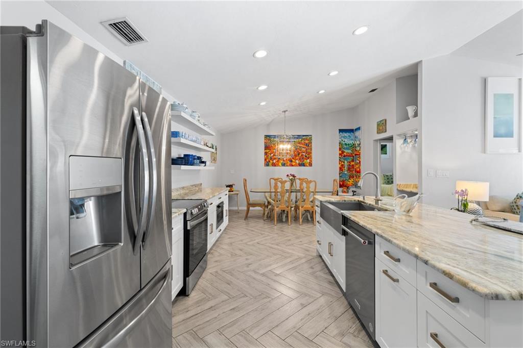 2467 Pinewoods Circle, Unit 3 Naples, FL 34105 - Photo 14 of 33 Kitchen featuring appliances with stainless steel finishes, light stone countertops, white cabinets, vaulted ceiling, and light parquet floors