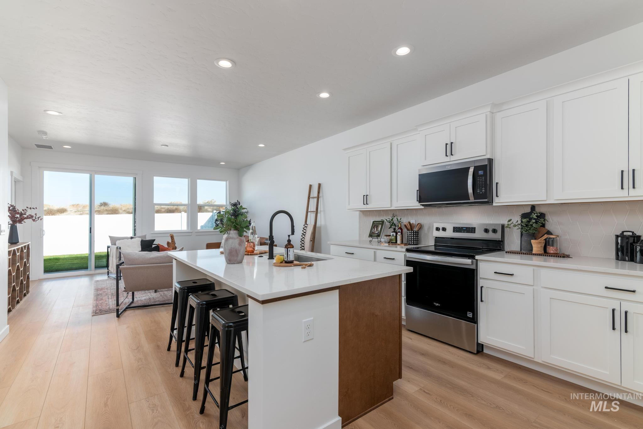 8521 West Stillmore Street Star, ID 83669 - Photo 4 of 7 Kitchen with white cabinetry, appliances with stainless steel finishes, a center island with sink, a kitchen breakfast bar, and light wood-type flooring