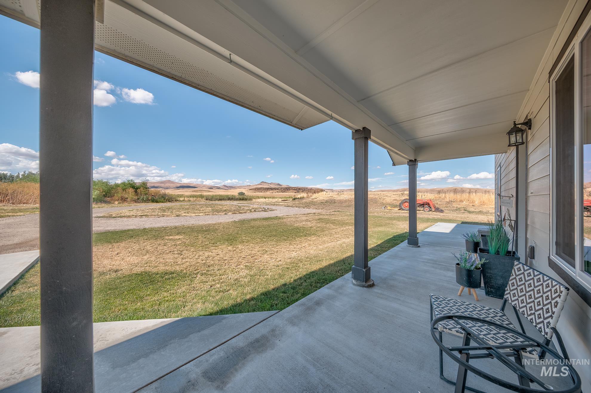 1049 Price Road Weiser, ID 83672 - Photo 32 of 47 Covered concrete porch extending the length of the home, featuring multiple support columns, a ceiling fan, and exterior wall lanterns