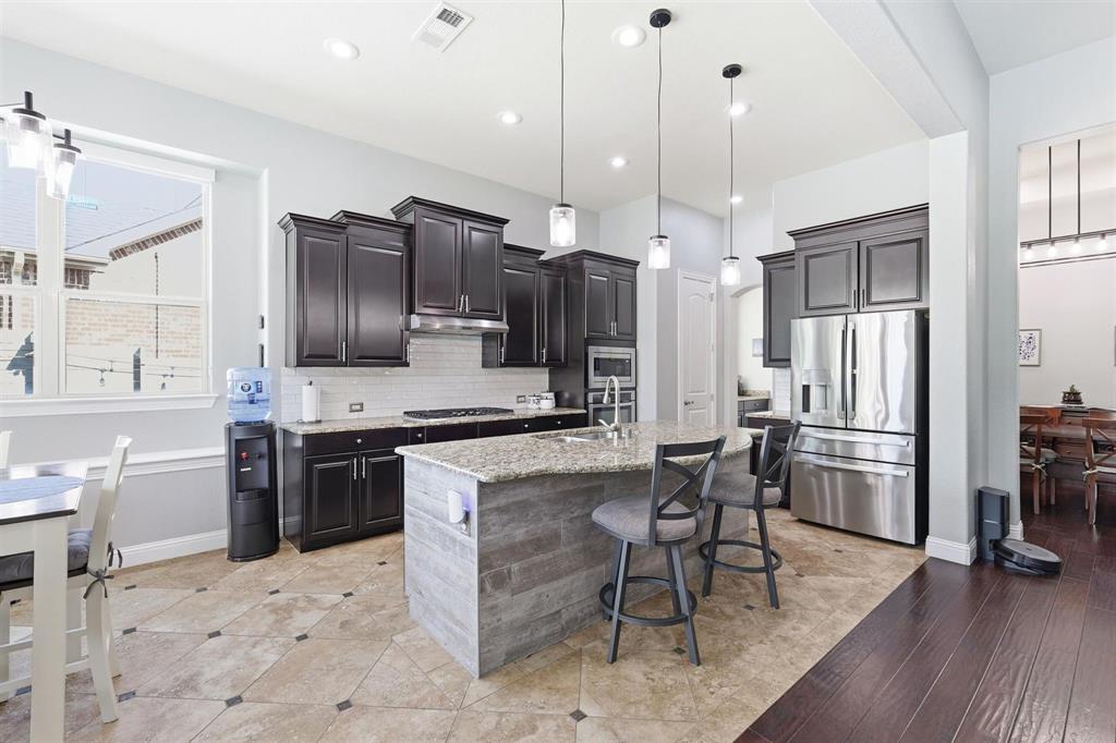 117 Birdcall Lane Argyle, TX 76226 - Photo 19 of 40 Kitchen with tasteful backsplash, appliances with stainless steel finishes, light stone countertops, a kitchen breakfast bar, and decorative light fixtures