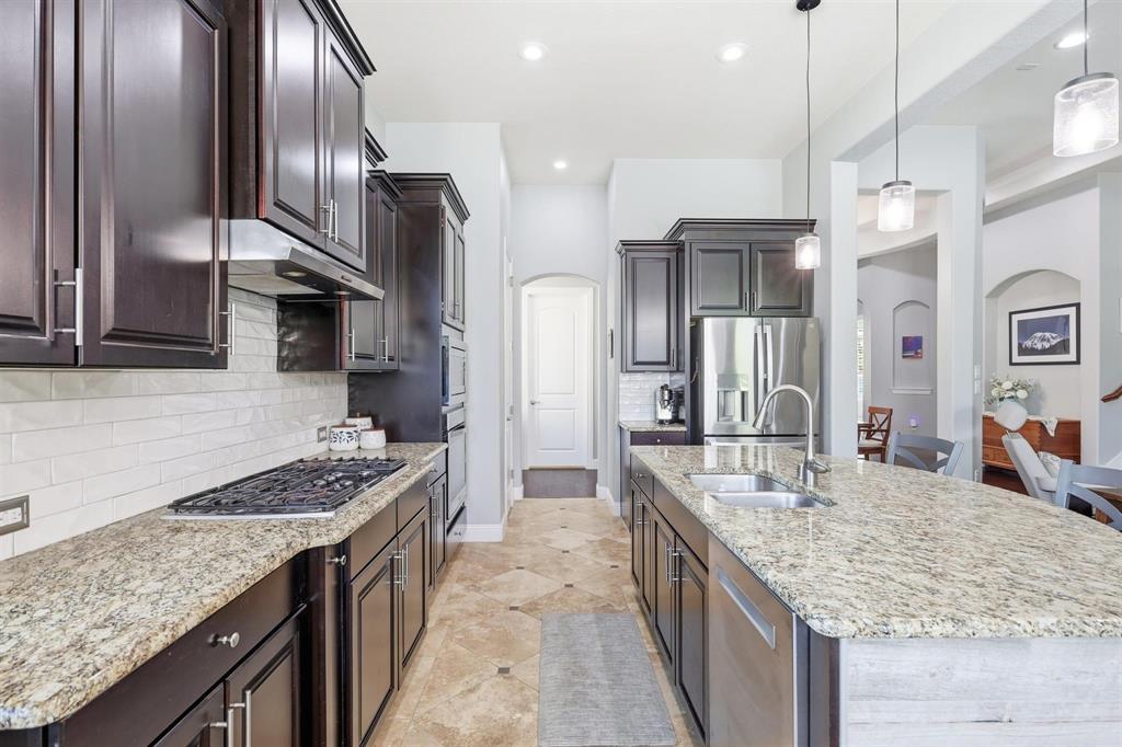 117 Birdcall Lane Argyle, TX 76226 - Photo 22 of 40 Kitchen featuring arched walkways, hanging light fixtures, decorative backsplash, appliances with stainless steel finishes, and light stone countertops